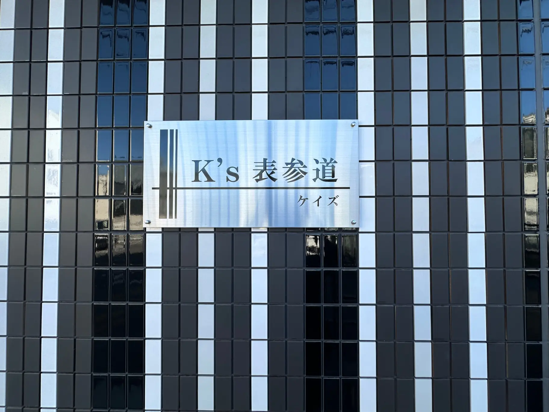 モノクロのタイル壁に取り付けられた「K's美容院」の看板