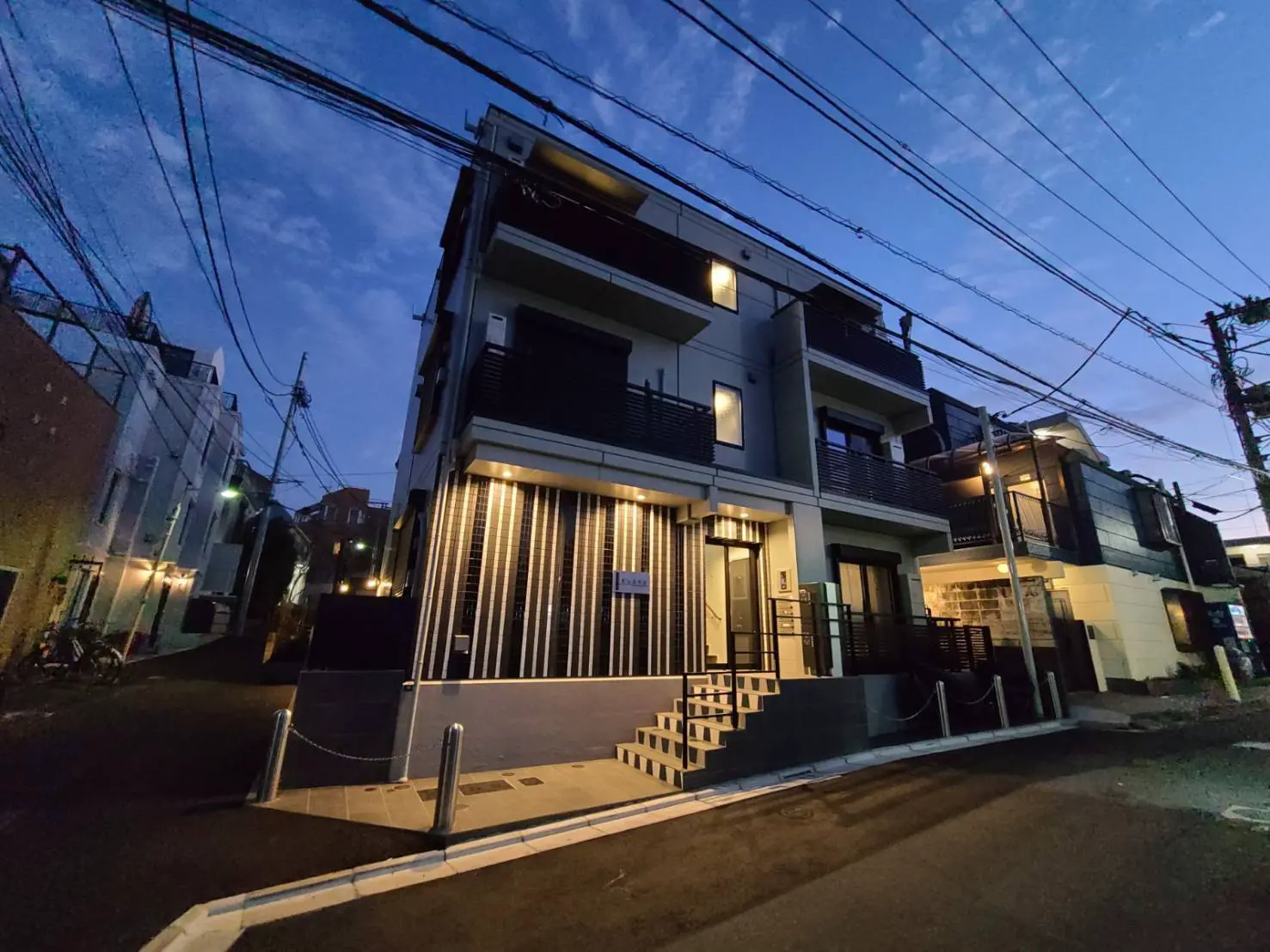 モダンな外観の新築住宅、夕暮れ時の街並み、電線が交差する住宅街の景色