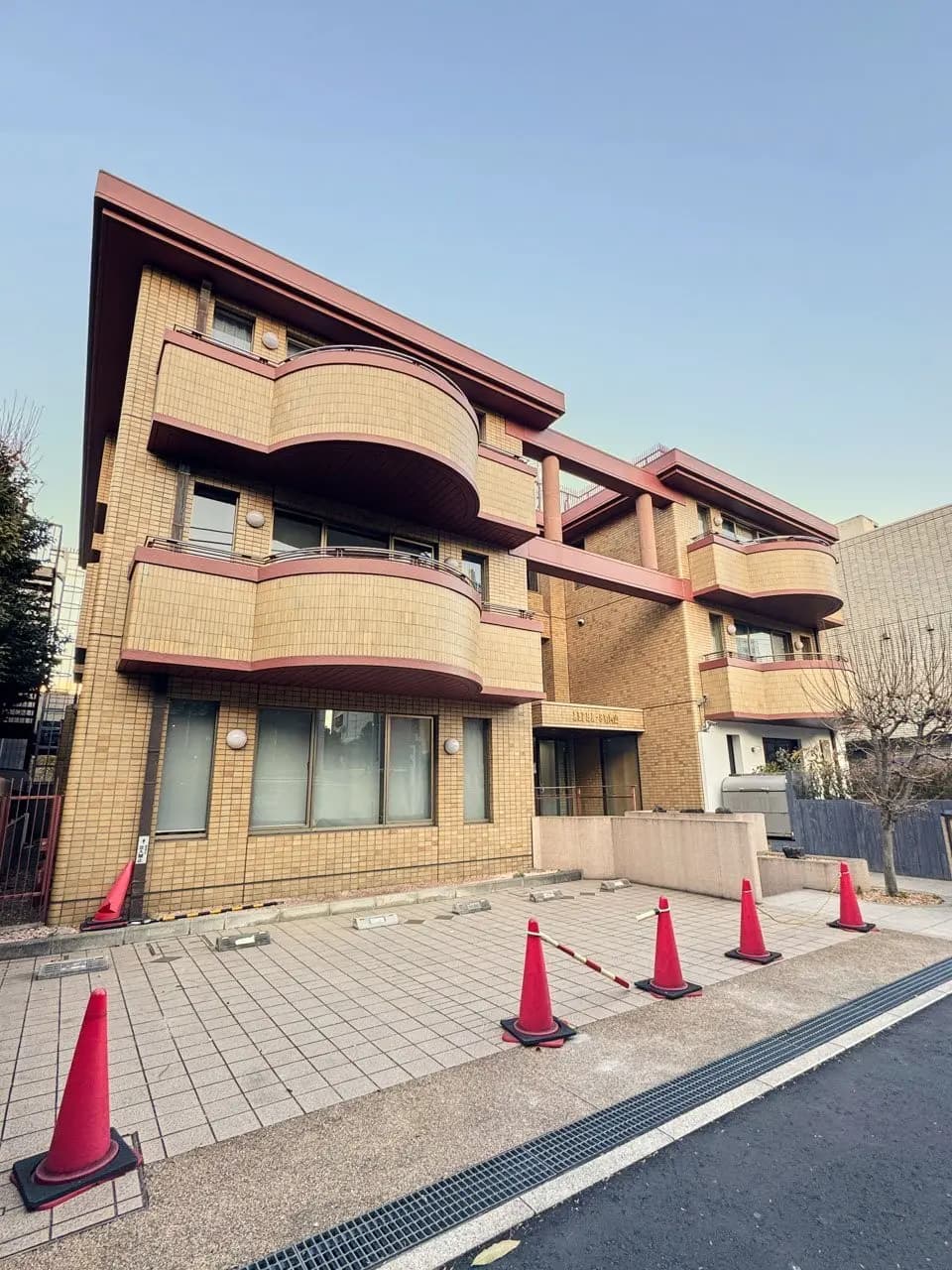 - モダンな外観のアパートメントビル、赤いコーンが置かれた舗装されたエリアと大きな窓が特徴のデザイン
