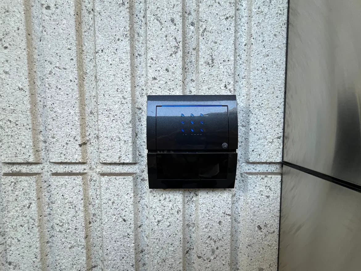 - コンクリート壁に取り付けられた黒いインターフォン、青いLEDライトが点灯しているシンプルなデザイン