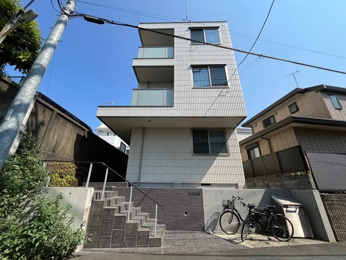 - モダンな外観の住宅、3階建てでバルコニーと大きな窓、傍に自転車と階段がある風景