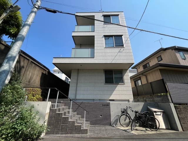 - モダンな外観の住宅、3階建てでバルコニーと大きな窓、傍に自転車と階段がある風景