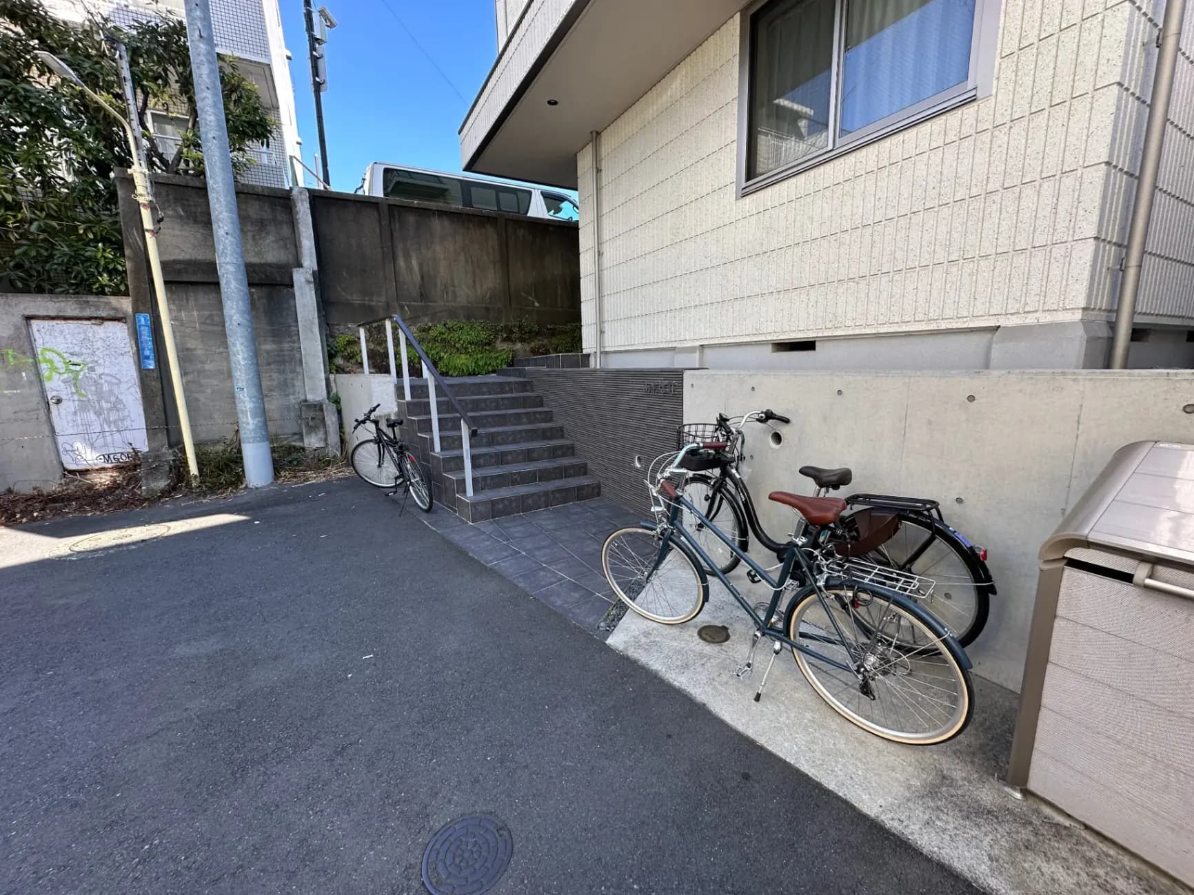 駐輪された自転車がある都市のアパートの入り口、階段とコンクリートの壁