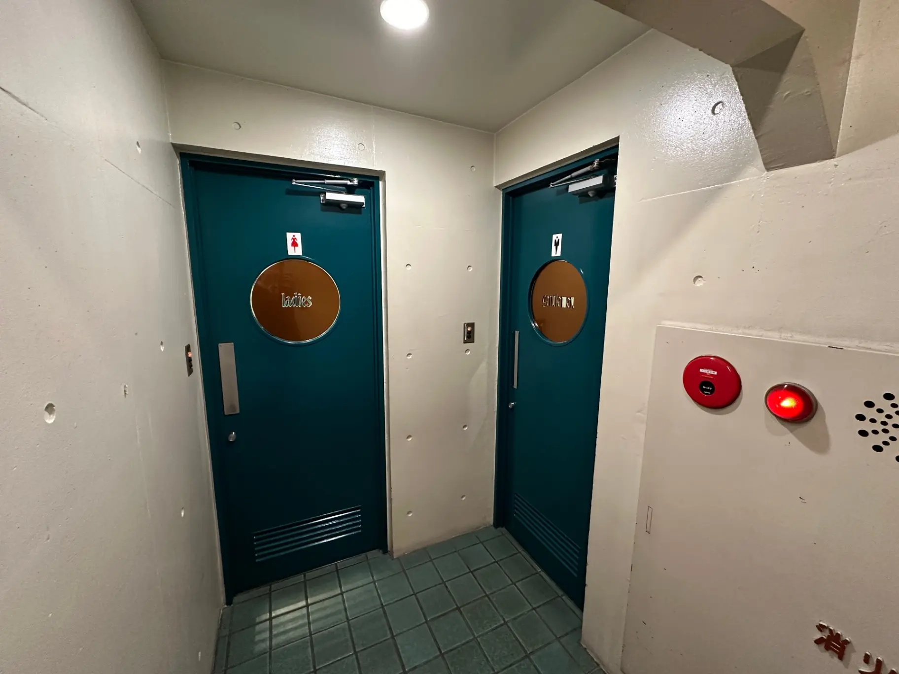 公共のトイレの入口、男女別のドアがある廊下、非常ボタンが壁に設置してあるインテリア