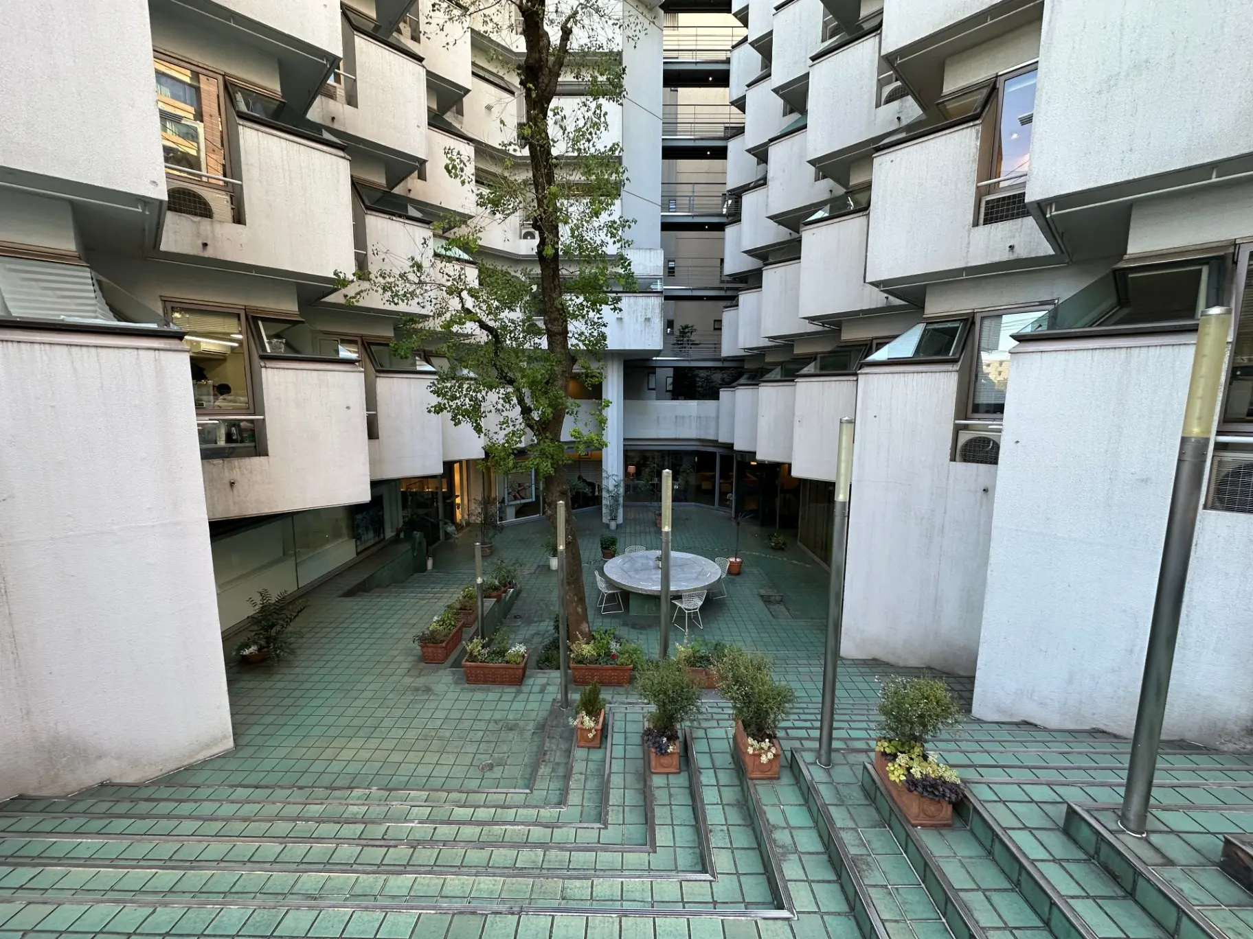 都市型マンションの中庭にある緑の植物とテーブル、角形のバルコニーが特徴的な共有スペース