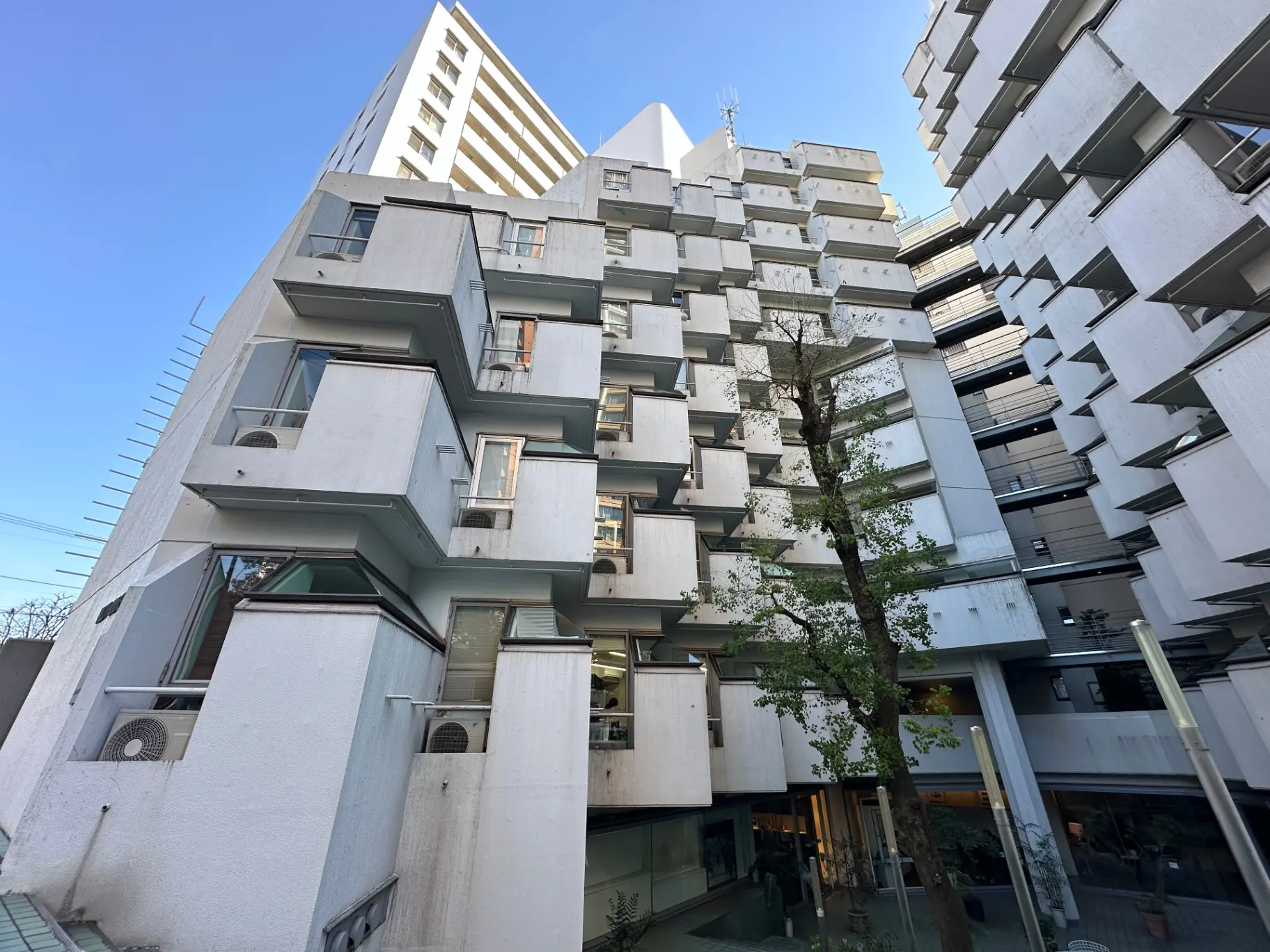 独特なデザインの都市型マンション、モダンな外観、立体的なバルコニー、中庭に植栽が見える