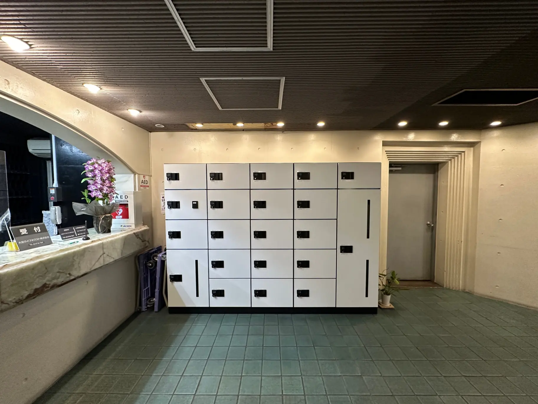 管理室と大型ロッカーが配置されたビルのエントランスホール、AEDと観葉植物を備えたインテリア