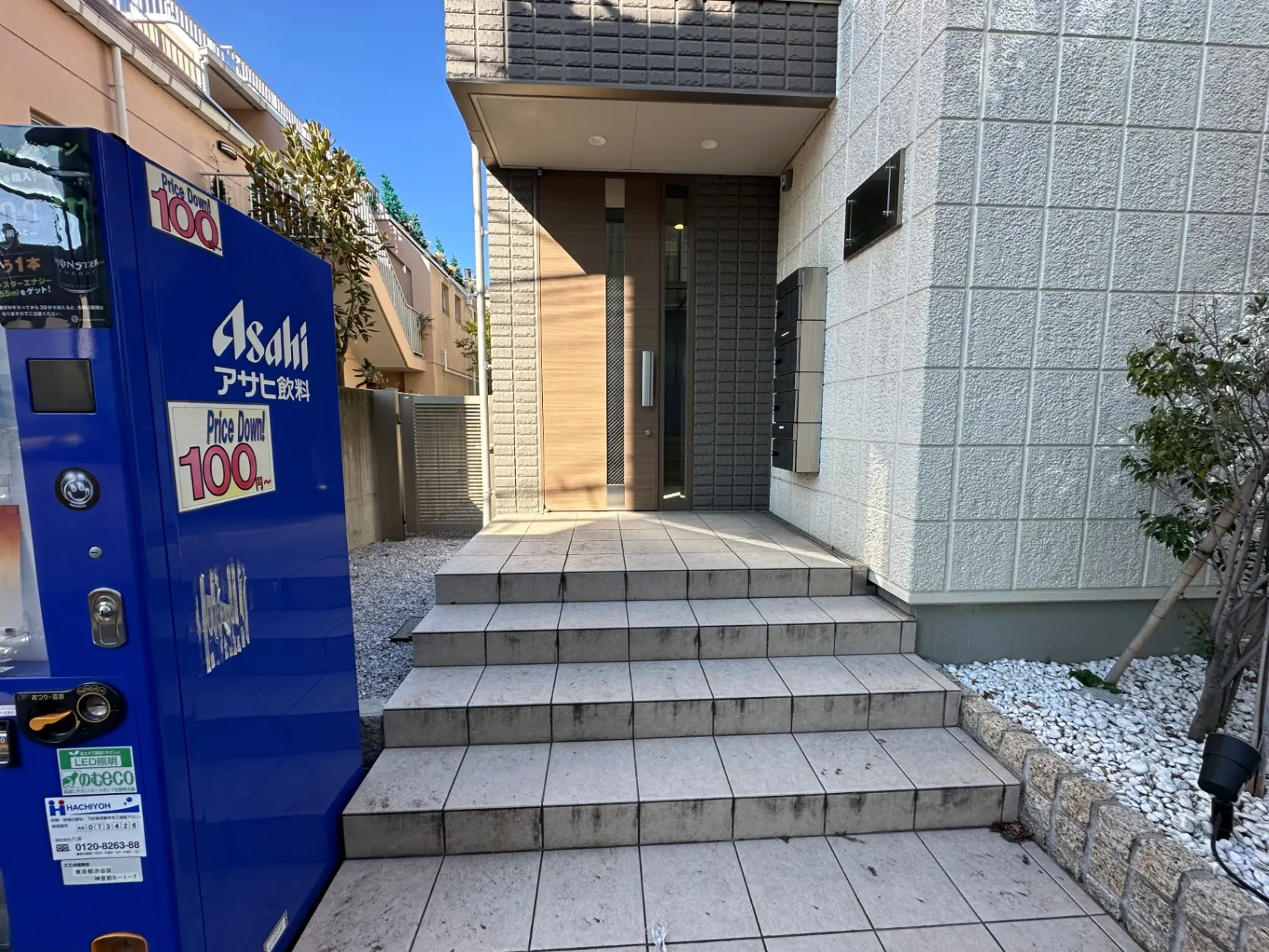清潔でモダンな住宅の玄関アプローチ、石造りの階段と植栽、左側に自動販売機