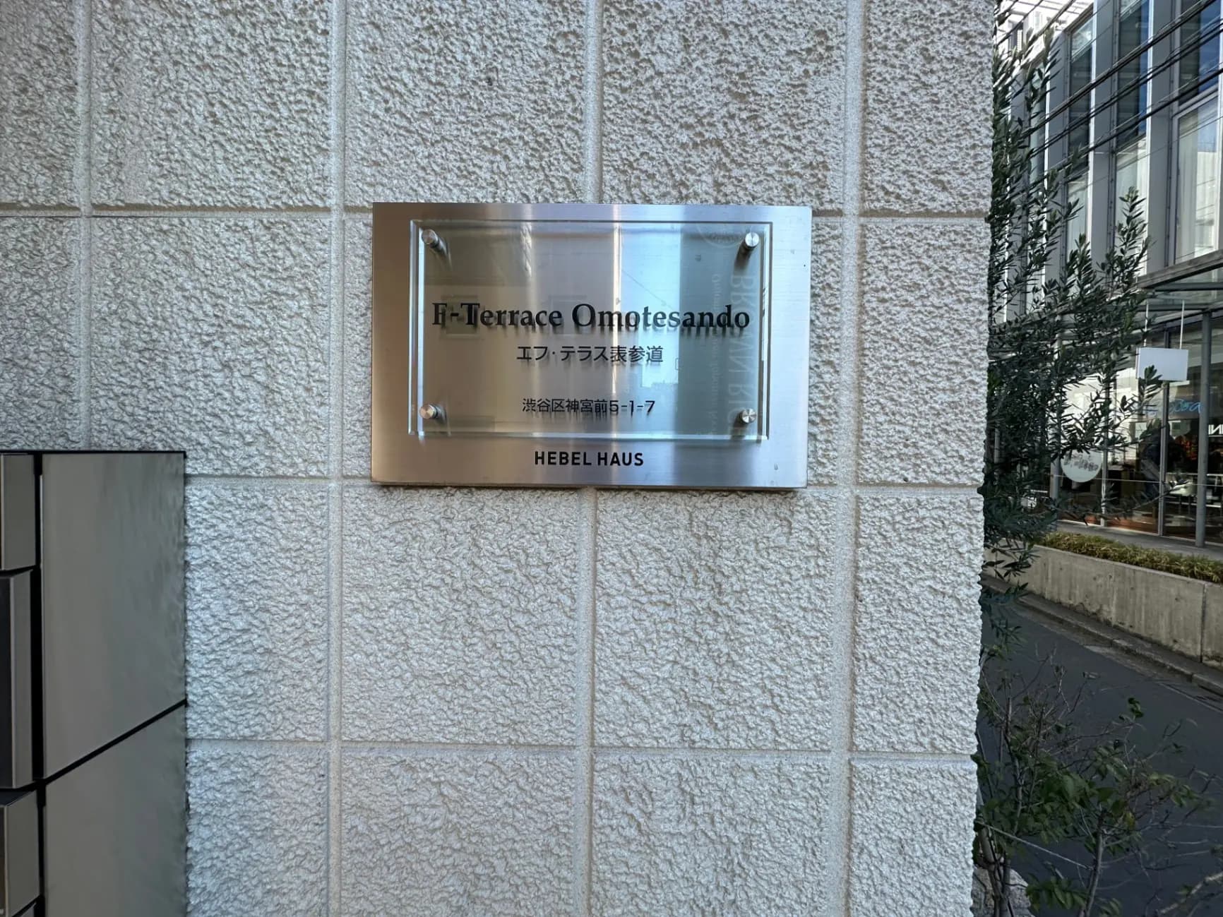 表参道にあるモダンなビルのエントランス看板、"H-Terrace Omotesando" のロゴが刻まれたステンレスプレート