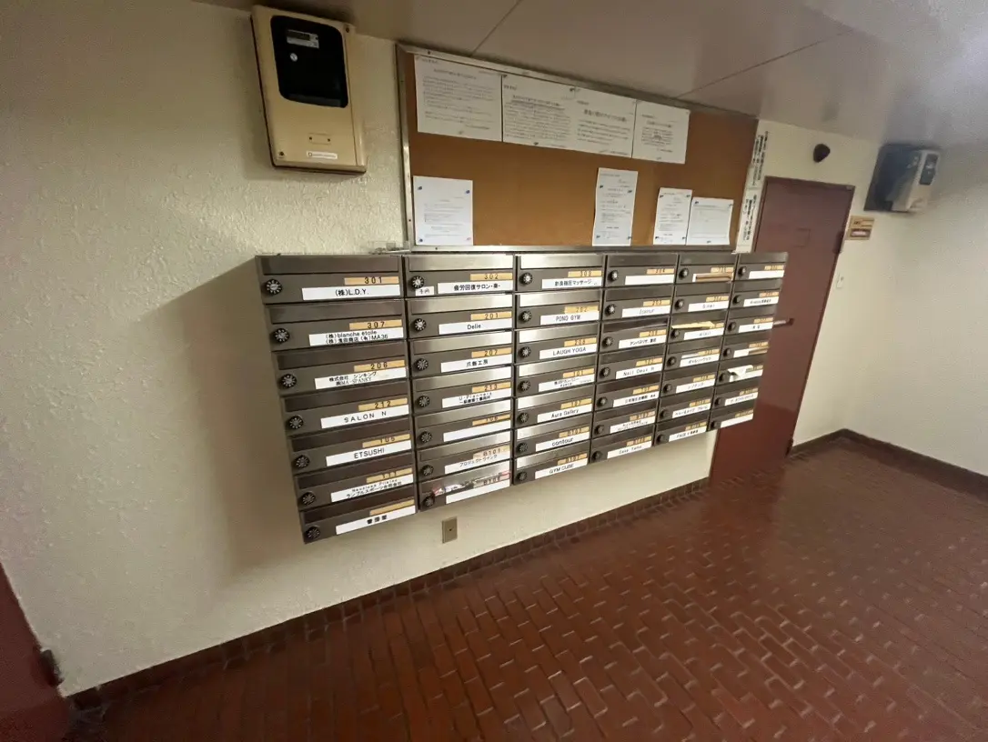 室内の郵便受けが並ぶ壁、案内掲示板とインターホンが設置されたエントリーホール