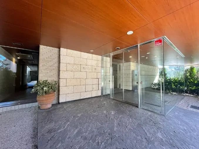 高級感のあるマンションのエントランス、ガラス製の自動ドアと木目調の天井デザイン