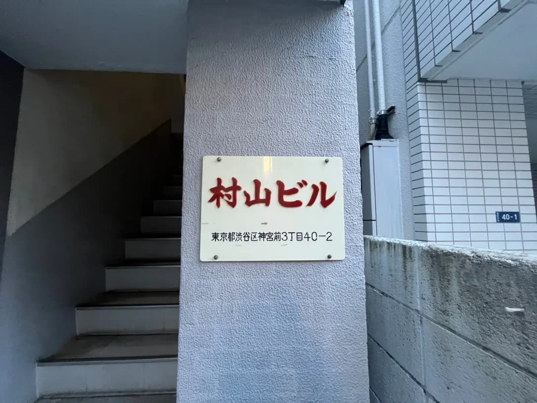 都会の建物の階段と壁に取り付けられた「紅しょうぶ」の看板、白い文字で住所が記載されている
