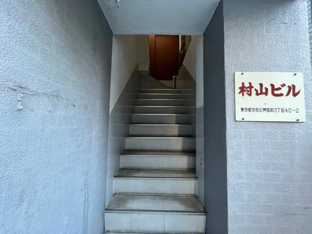 狭い入り口の階段と壁に取り付けられた「納屋ビル」と書かれた看板