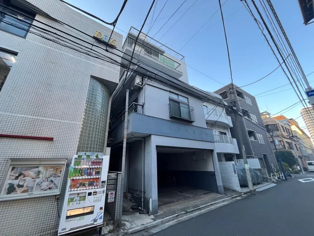 街角にあるモザイクタイルの壁面建築、設置された自動販売機、地上からの配電線が見える市街地の風景