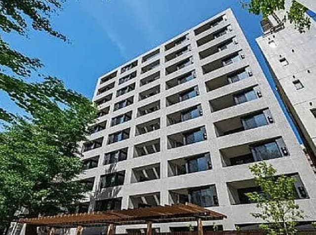 - モダンなデザインのアパートメントビル、青空を背景にした6階建ての外観、周囲に緑の木々がある景観