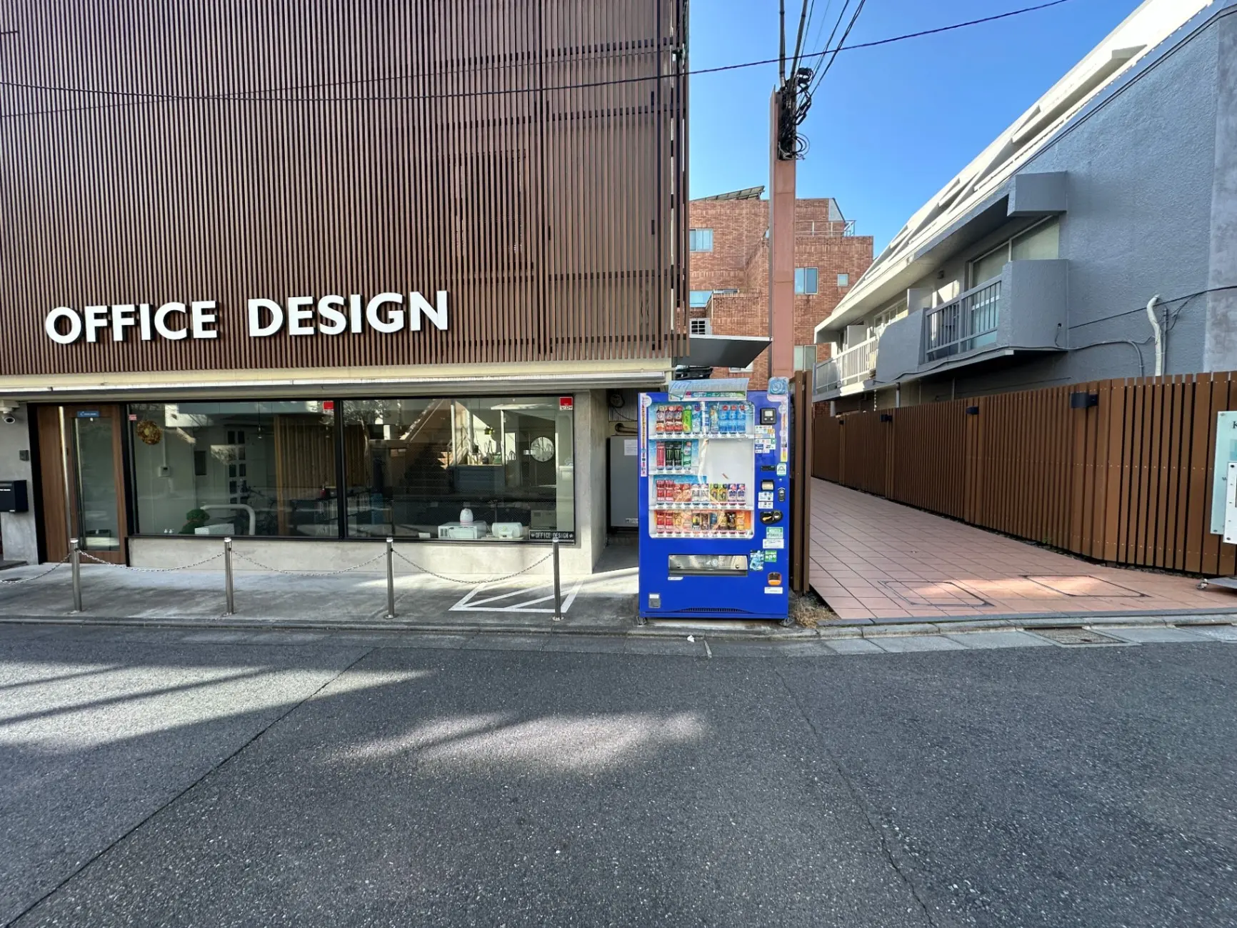 オフィスデザインのサインが掲げられたビル、路上に設置された自動販売機、晴れた日の都市風景