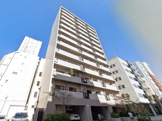 - 青空の下にそびえるモダンなマンション、周囲に他の建物と駐車場がある都市風景