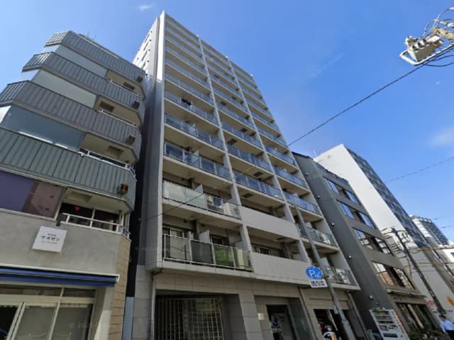 - 都会的な景観の中にそびえる高層マンション、隣接する建物と青空が見える風景