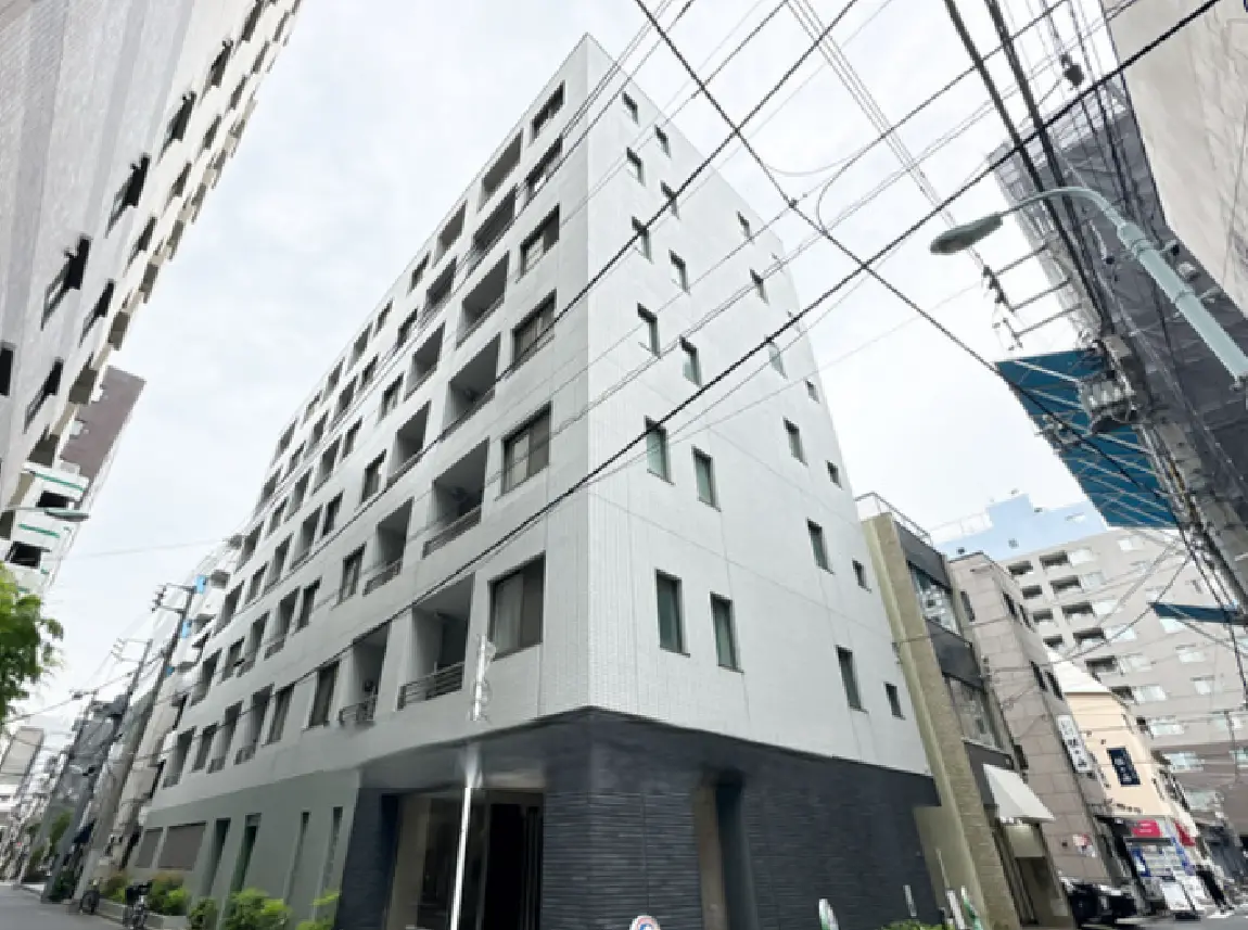 - 現代的な外観の集合住宅、グレーのタイル張りで大きな窓が並ぶデザイン、周囲には電柱や他の建物が立ち並ぶ街並み