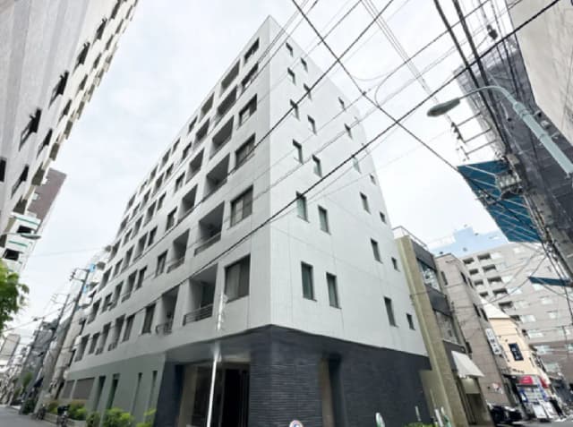 - 現代的な外観の集合住宅、グレーのタイル張りで大きな窓が並ぶデザイン、周囲には電柱や他の建物が立ち並ぶ街並み