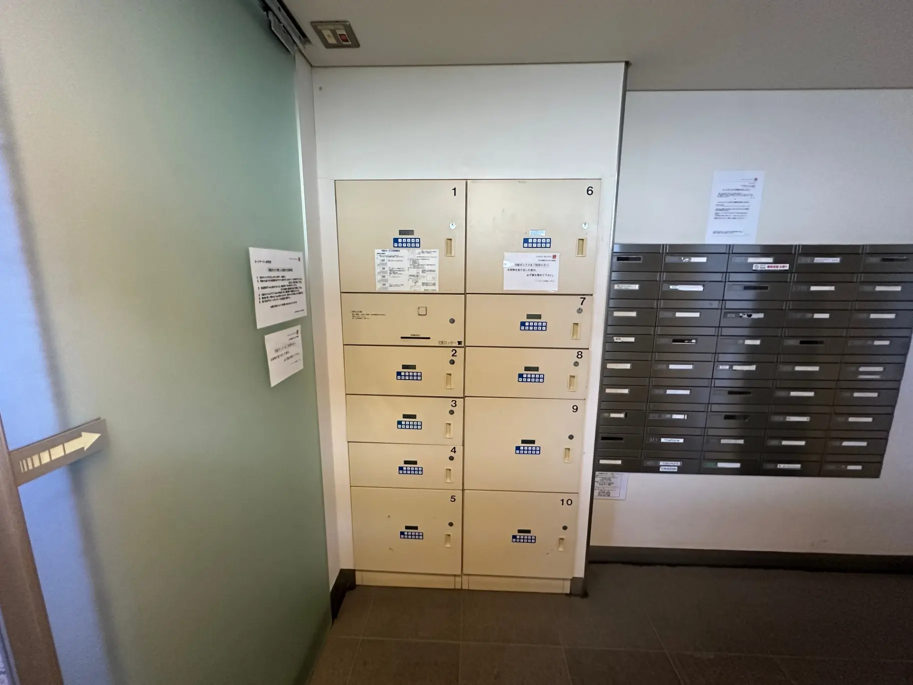 マンションのエントランスに設置された郵便受け、番号付きのロッカーと多数のポストが並ぶ内装
