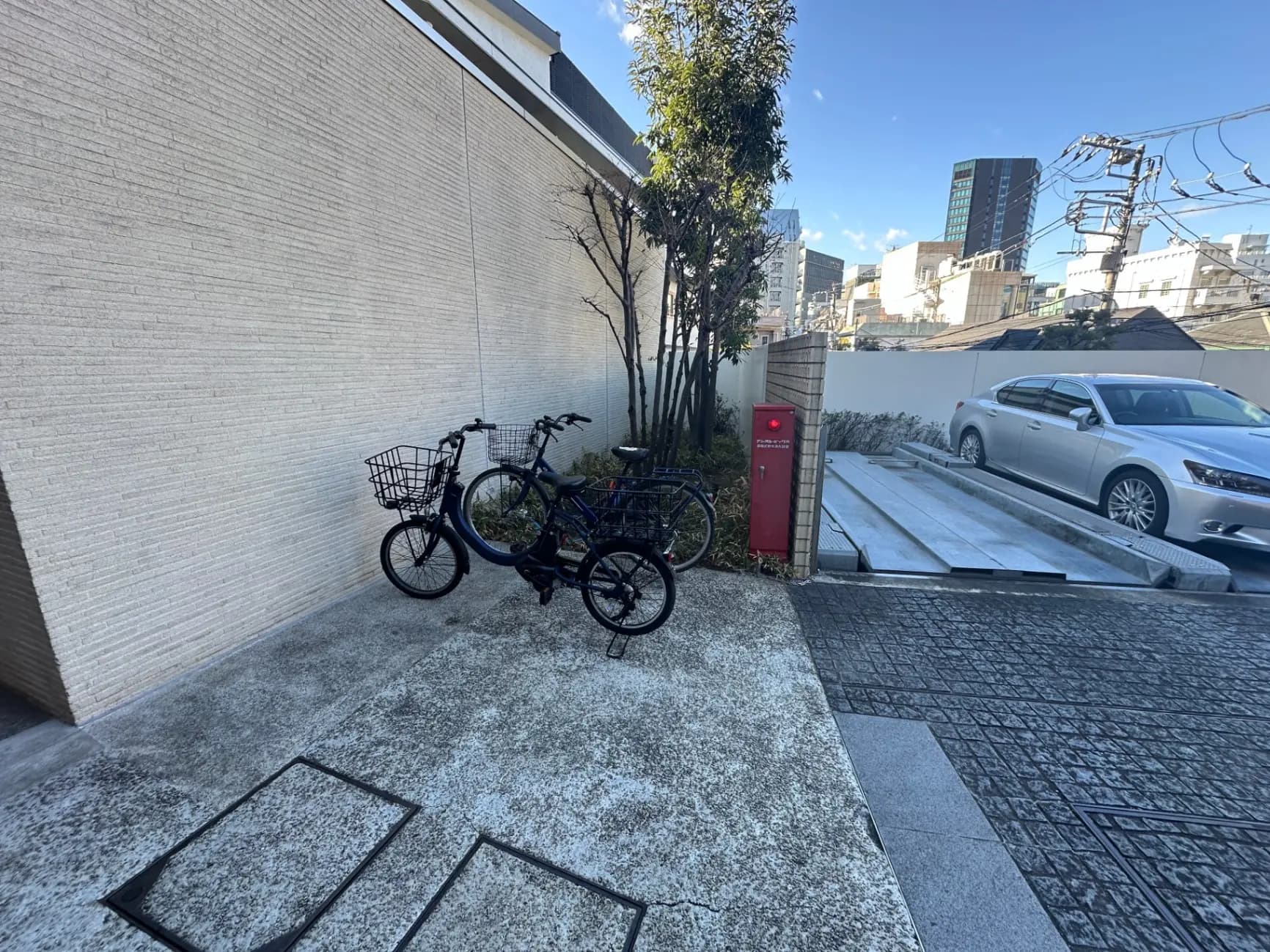 都会の駐輪場に止められた自転車、白い壁と植木、背景にビルと自動車