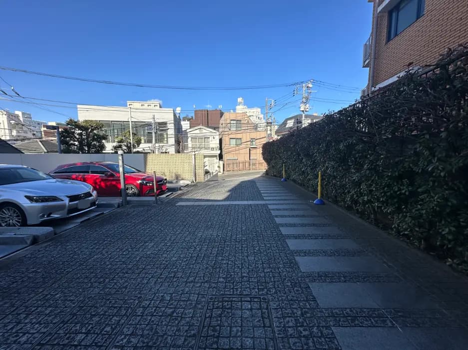 都会的な雰囲気の駐車場、建物と緑の生け垣、晴れた日の青空