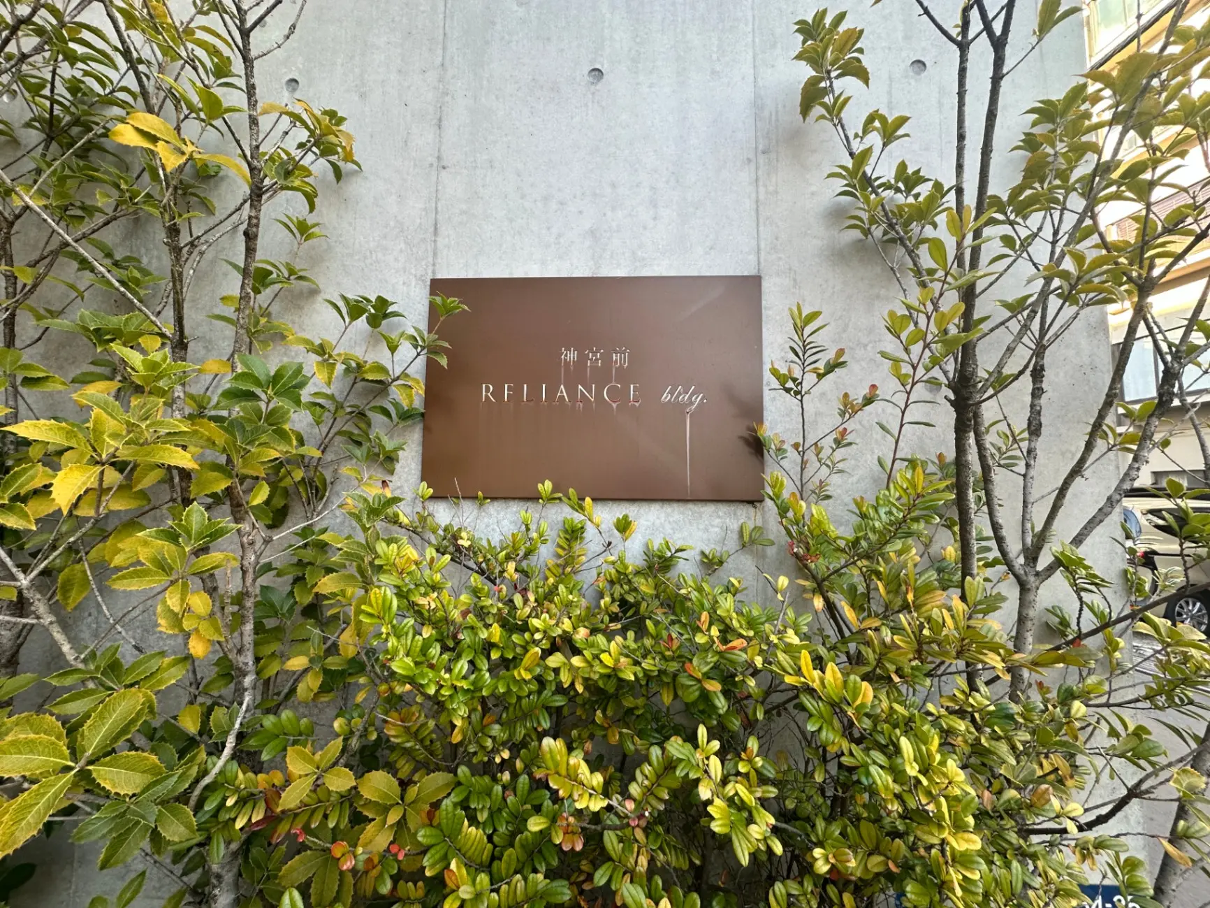 緑豊かな植栽の前に掲げられた「REFIANCE bldg.」の茶色い看板
