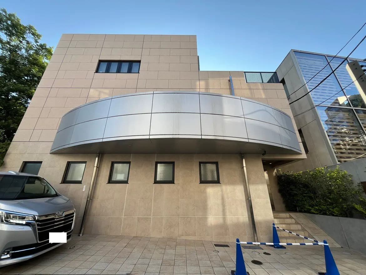 - モダンな外観の建物、曲線的な屋根と大きな窓、近くに停車中の車と駐車場のコーンが見える景観