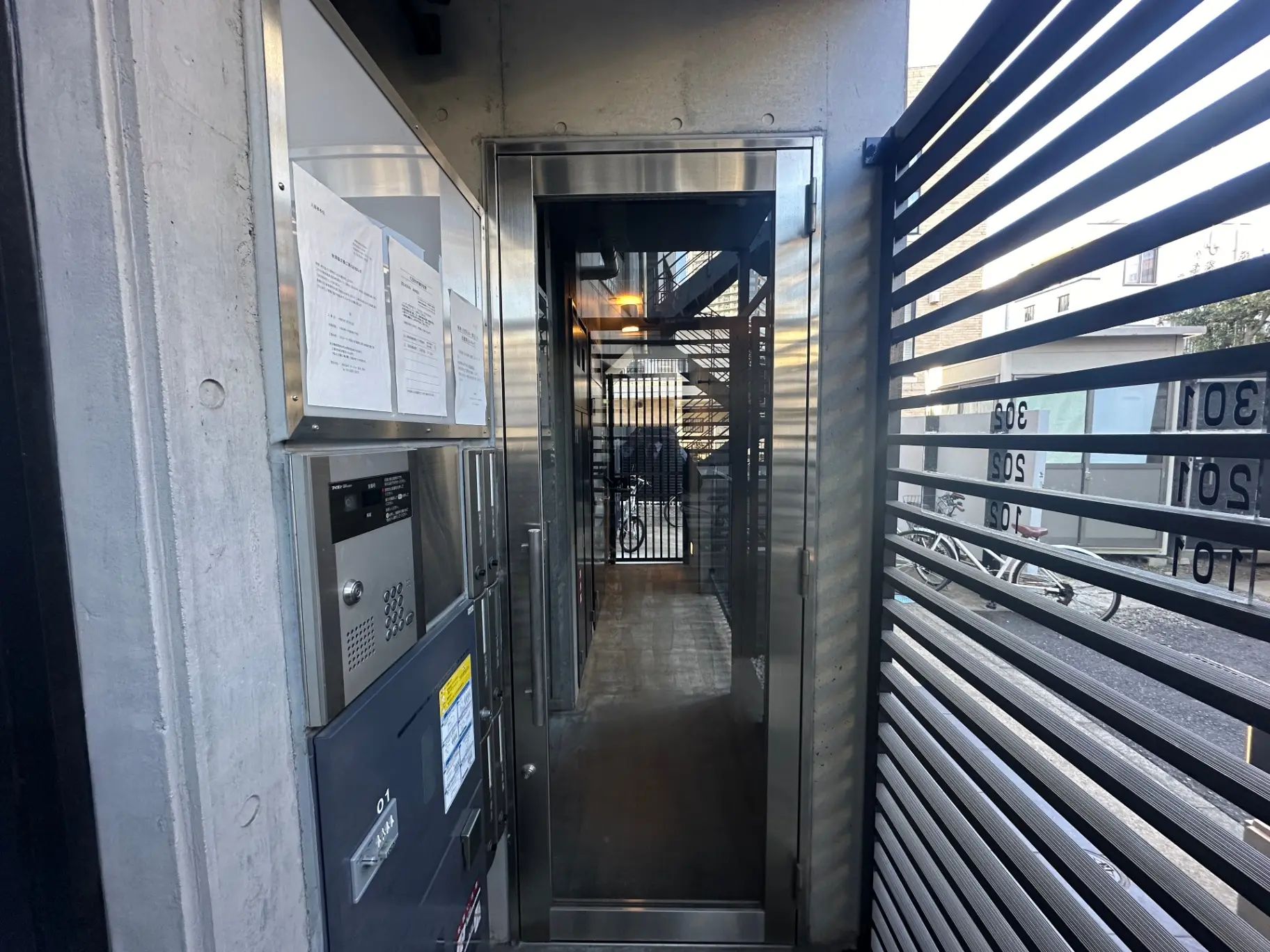 モダンな建物のエントランス、インターフォンと郵便受け、金属製の門扉と都会的な雰囲気