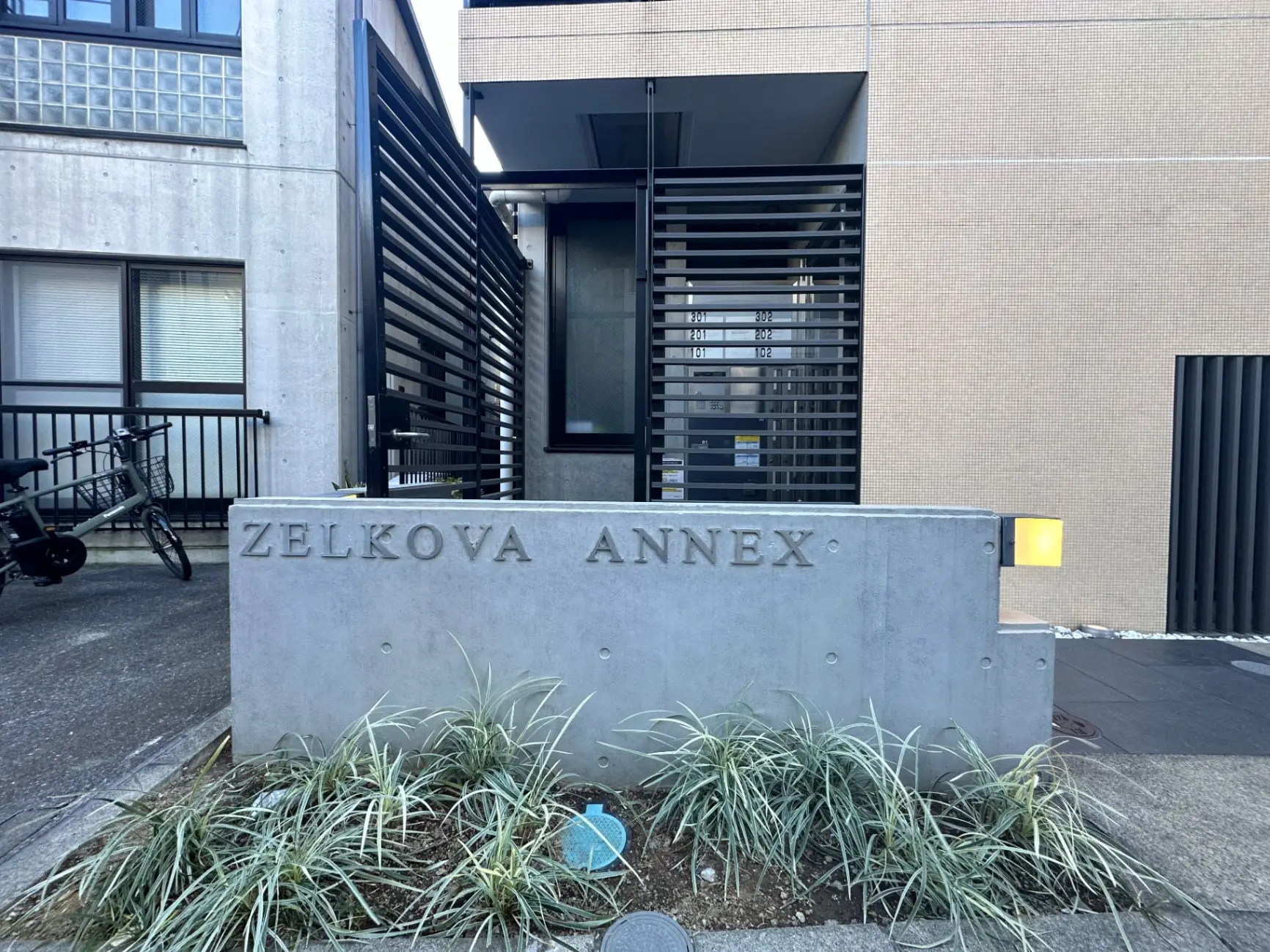 モダンで洗練された外観のZELKOVA ANNEXビルのエントランス、コンクリート製の看板と黒い格子状のフェンス