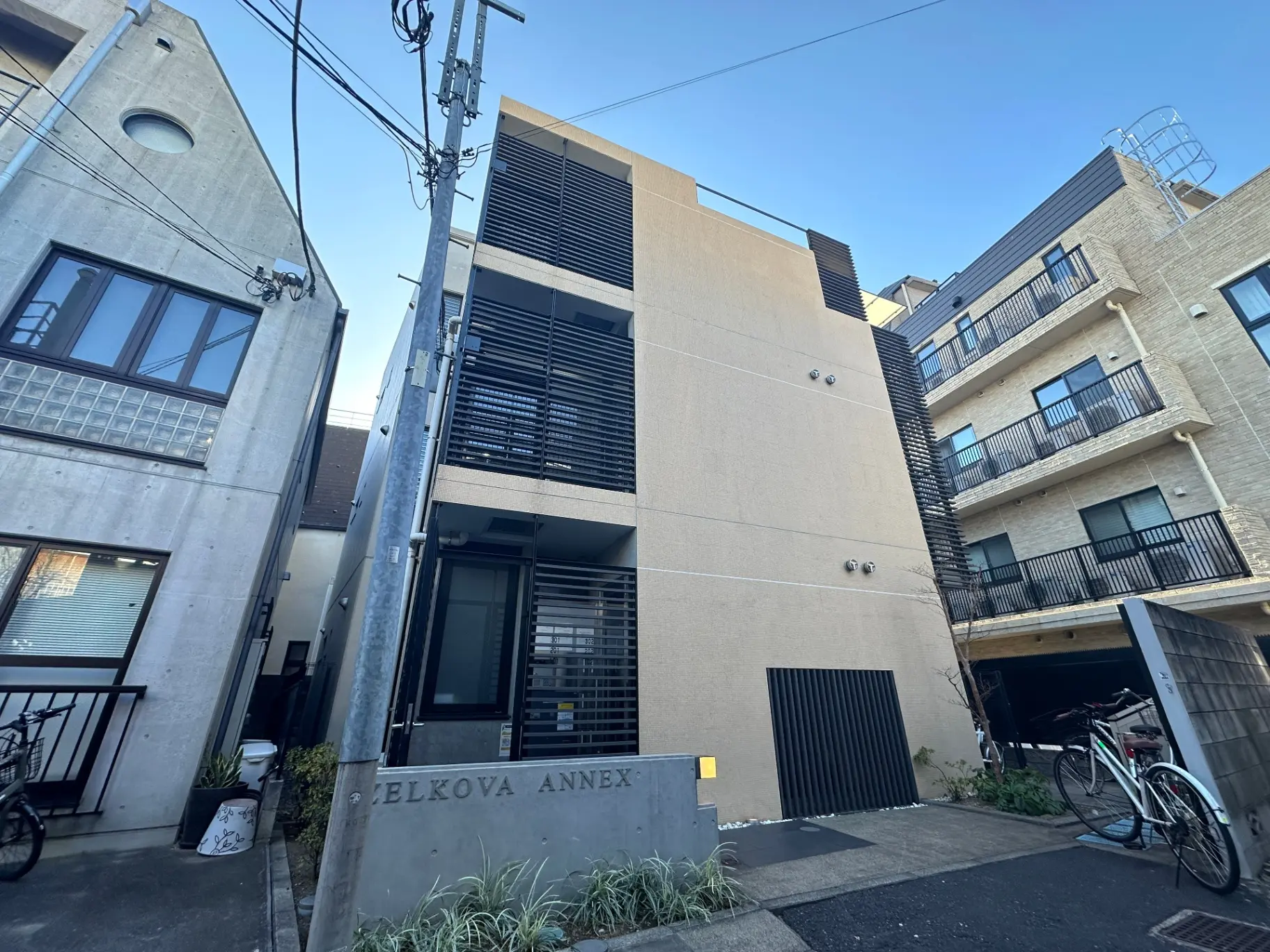 現代的なデザインのアパート外観、エルコバアネックスの看板、自転車が置かれたエントランス