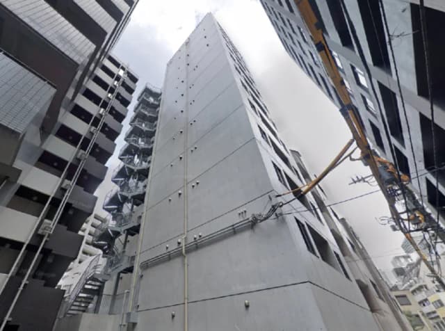 - 複数の高層ビルに囲まれたコンクリート製の建物、外部は無機質なデザインで、階段と配管が目立つ構造