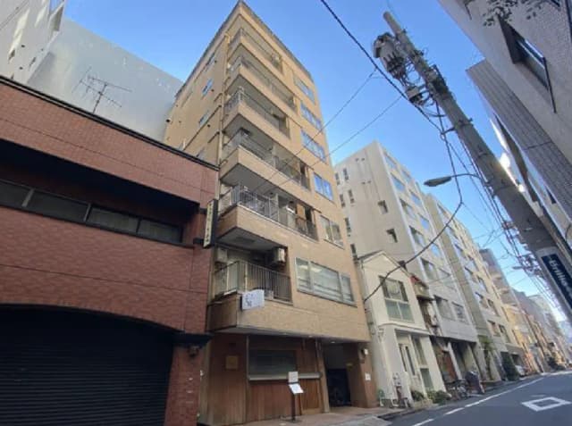 - 東京都内のアパートメントビル、明るい外観とバルコニーが特徴的、周辺には他のビルが立ち並ぶ建築風景