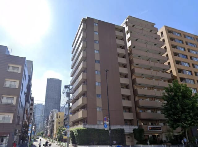 - 都市の高層ビル群の中に立つモダンなマンション、青空の下での外観、バルコニー付きの住宅街の風景