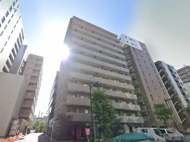 - 明るい日差しが映える高層マンションの外観、隣接するビルと緑豊かな街路樹がある風景