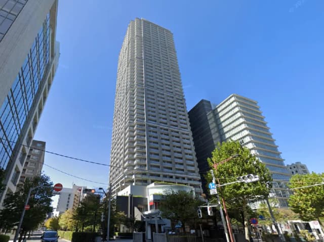 - 高層ビルとオフィスビルが並ぶ都市景観、青空の下で緑豊かな街路樹が映える風景