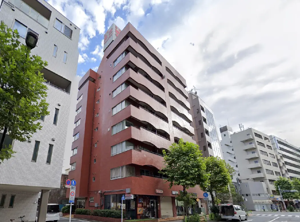 - 現代的なデザインの赤い建物、周囲には緑豊かな街路樹とその他の商業ビルが並ぶ風景