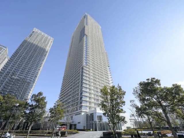- 近代的な高層ビル群、青空の下に聳え立つガラス張りのタワーと周囲の緑豊かな公園風景