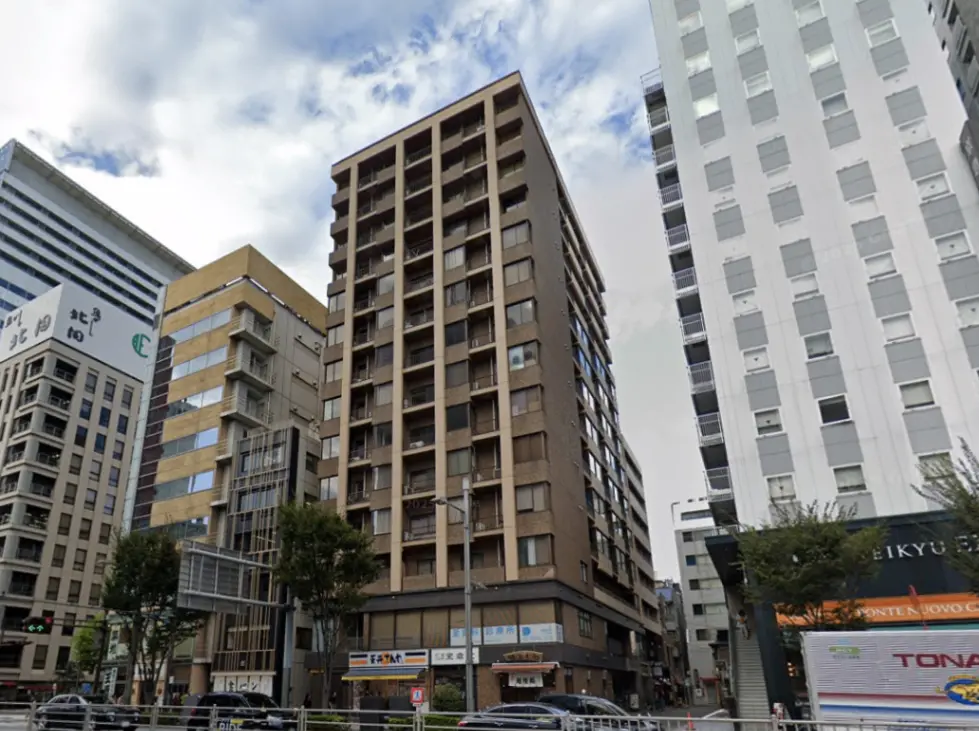 - 都市のビル群の中に位置する多層住宅、隣接するオフィスビルと商業施設が見える風景