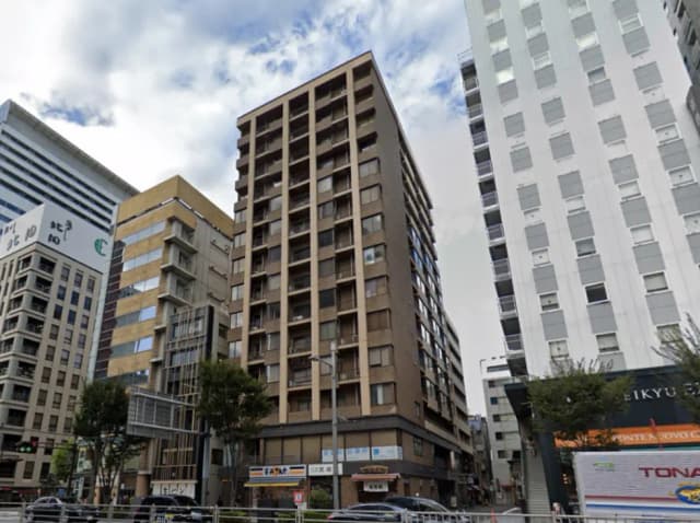 - 都市のビル群の中に位置する多層住宅、隣接するオフィスビルと商業施設が見える風景