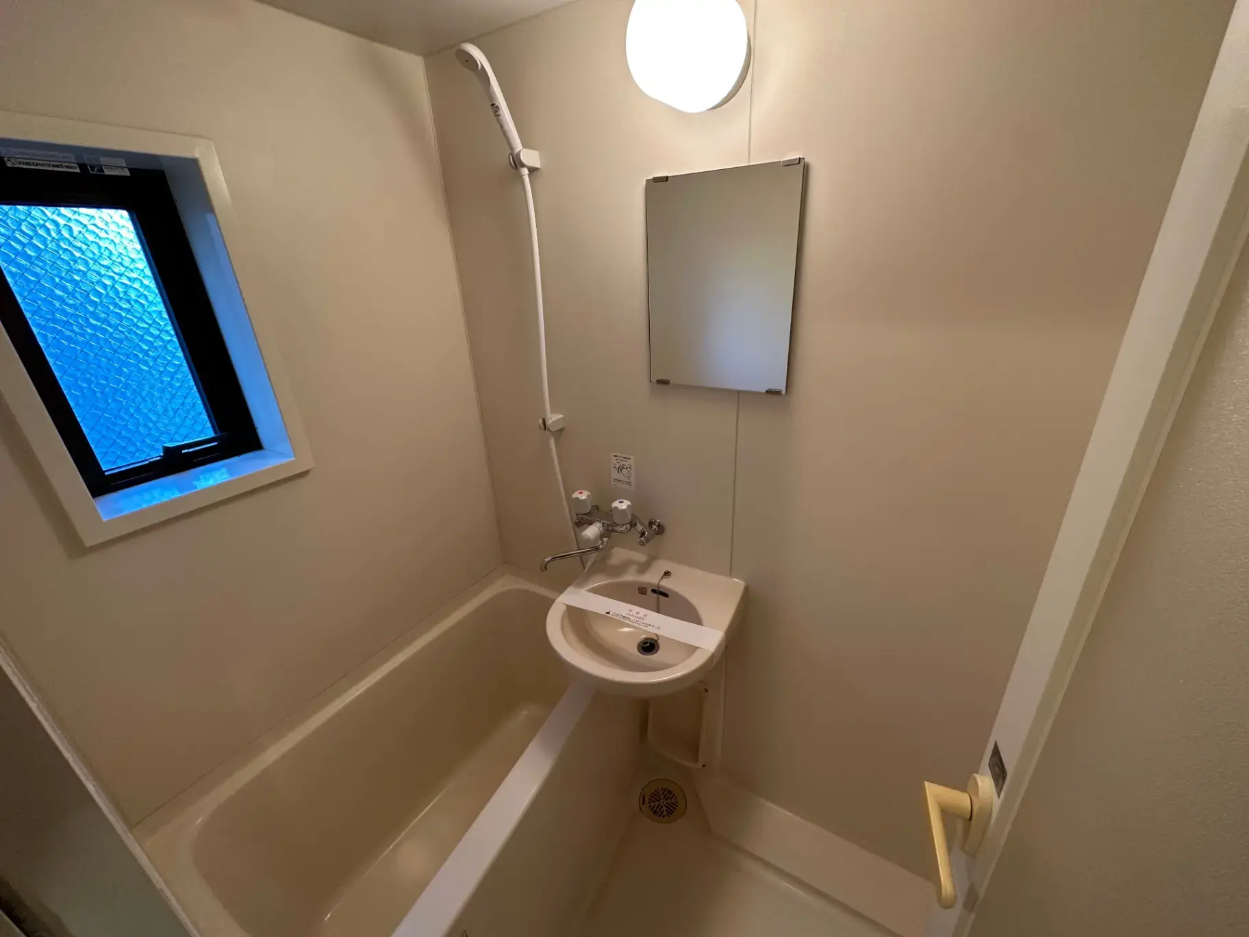 コンパクトな浴室に一体型洗面台と浴槽、蛍光灯照明と小窓が付いた清潔感のある空間