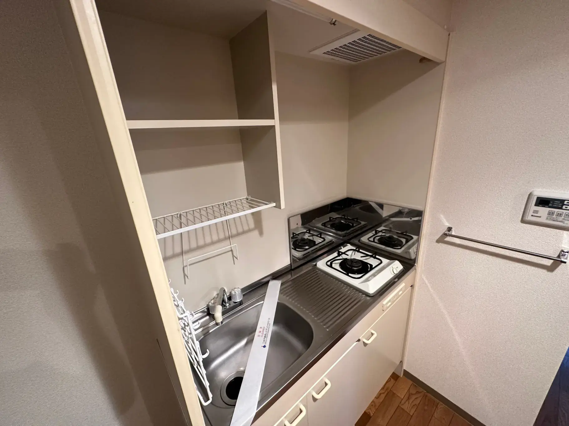 二口ガスコンロ付きのコンパクトなキッチン、収納棚と換気扇完備