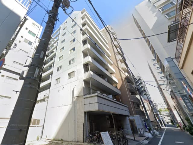 - 都心部に位置する現代的なマンションの外観、隣接するビルや電柱が映る通りの風景