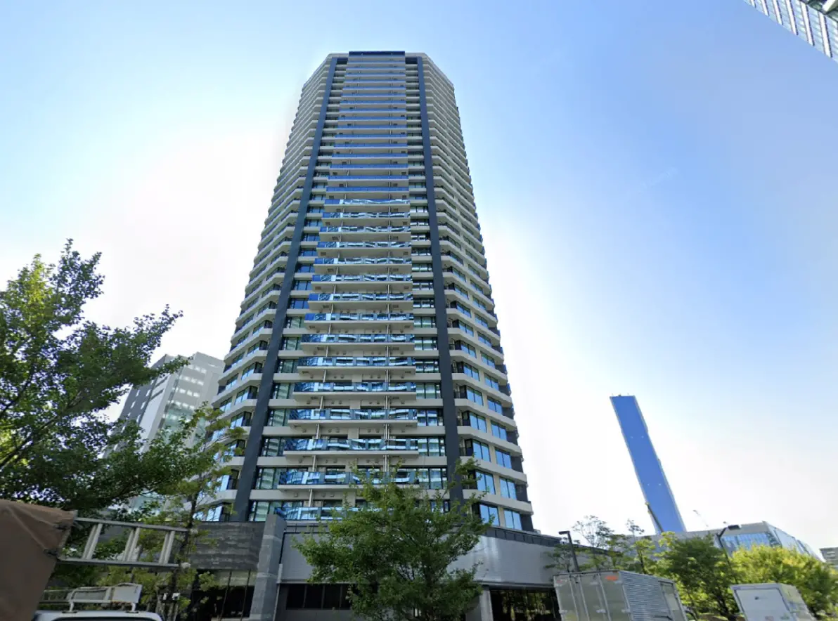 - 高層ビルの外観、ガラス張りのバルコニーを持ち、青空の下でそびえ立つ新しいコンテンポラリー建築。周囲に緑豊かな樹木が並ぶ。