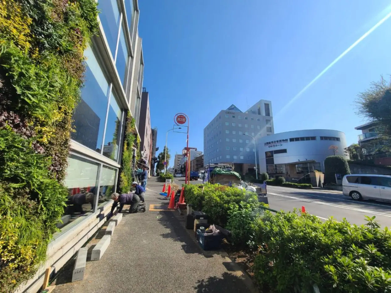 日差しが降り注ぐ都市の通り、緑豊かな壁面緑化を施したモダンなビルのメンテナンス作業