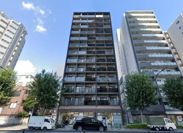 - 都市型の高層マンションの外観、隣接する建物や青空が映える街並み、植栽が施された歩道の風景