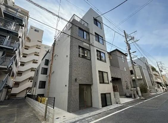 都市の住宅街に建つ現代的なデザインのアパートメント外観、グレーの壁面とシンプルなファサードデザイン