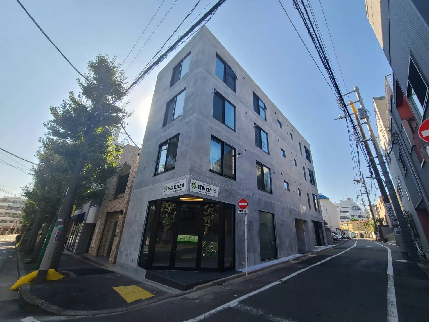 現代的なデザインの新築ビル、青空の下で道路隅に位置し、ガラス窓とコンクリートのファサードが特徴的な外観