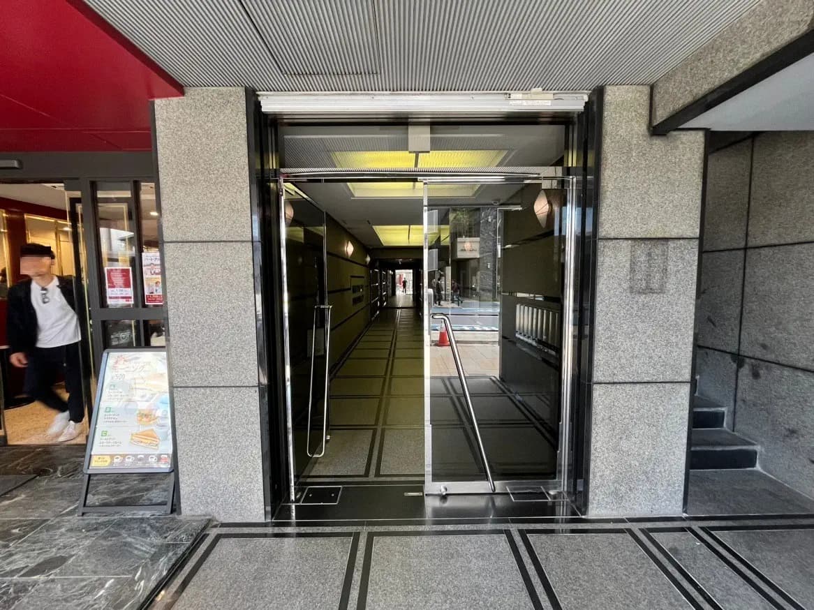 ビルのエントランスと自動ガラスドア、通路にメニュー看板が置かれたレストランの入口